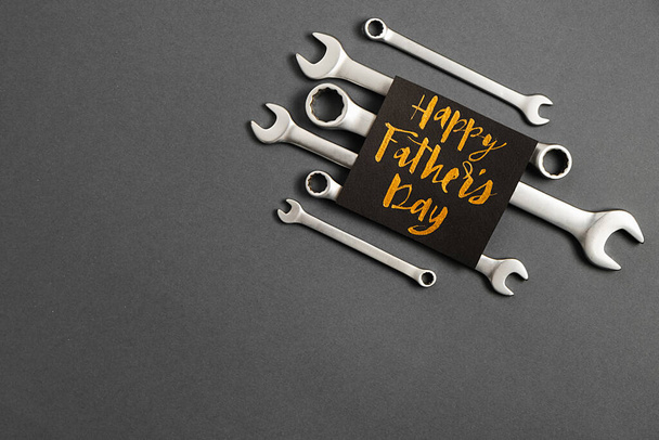 Creative flat lay composition with combination wrenches, card with phrase happy father's day and retro stylish black paper photo booth props moustaches on grey studio background wall. Space for text - Zdjęcie, obraz