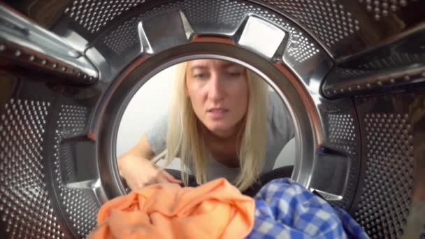 Smelly washing machine and laundry room. Young blonde woman looks inside washing machine, smells stench and plugs her nose. View from inside drum at wide angle. odor elimination. Young hostess. - Felvétel, videó