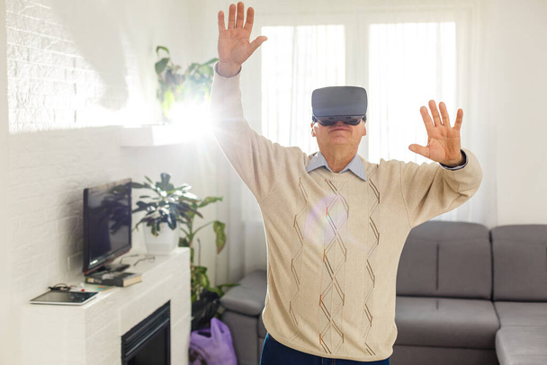 Elderly man wearing a Virtual Reality glasses at home - Photo, Image