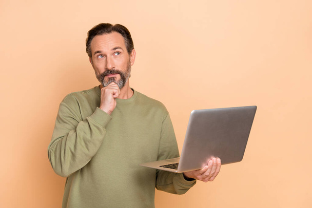 Portrait of attractive minded skilled man using laptop deciding copy space isolated over beige pastel color background - Photo, Image