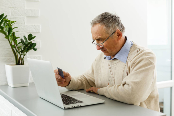 Vanhempi mies kotona kytketty kannettavaan tietokoneeseen
 - Valokuva, kuva