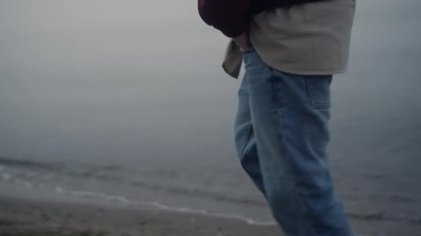 Nierozpoznany człowiek spacerujący po plaży morskiej. Facet trzyma się za ręce w jeansach kieszenie zbliżenie - Materiał filmowy, wideo