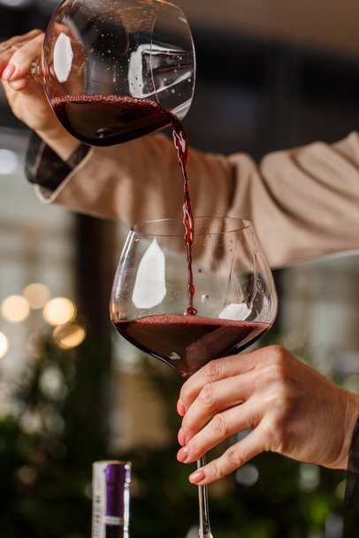 Male hand holds beautiful clear stemware for burgundy wine into which red wine is poured from another stemware - Фото, изображение