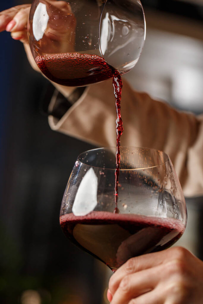 Male hand holds beautiful clear stemware for burgundy wine into which red wine is poured from another stemware - Foto, Bild