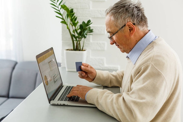 Bilgisayardaki kıdemli adam online alışveriş için kredi kartıyla ödeme yapıyor. - Fotoğraf, Görsel