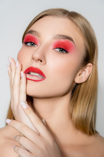 Young model with red makeup looking at camera isolated on grey  - Foto, Imagen