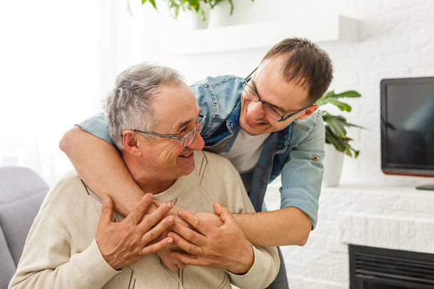 Χαρούμενος συνταξιούχος άντρας και ενήλικος γιος μιλάνε στο σπίτι - Φωτογραφία, εικόνα