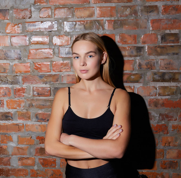 sport and yoga lifestyle concept. Young fit pretty woman dressed in sport clothes poses against brick wall. - Фото, зображення