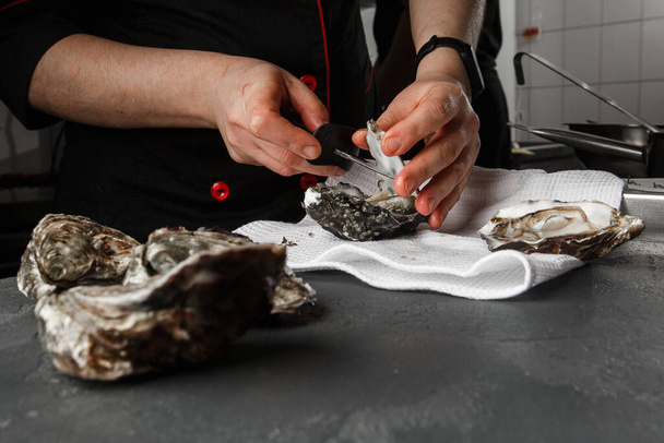 Someone shucking an oyster as water drips out of it. The oyster opening is in focus and the persons hands and background are out of focus. - 写真・画像