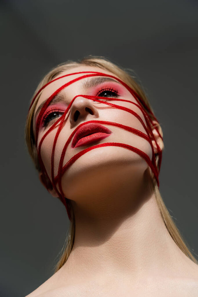 Low angle view of woman with red makeup and threads isolated on grey  - Fotoğraf, Görsel