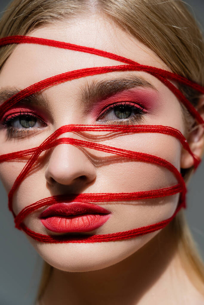 Portrait of young model with lips and threads on face looking at camera isolated on grey  - Foto, imagen