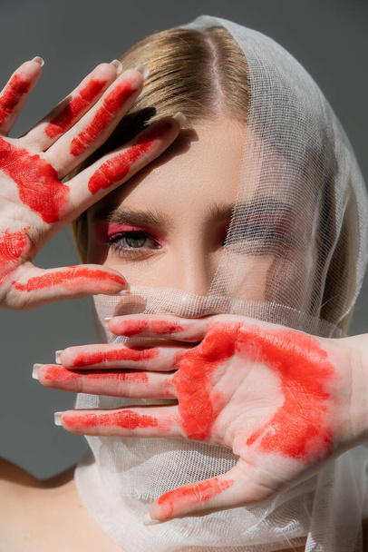 Model with medical bandage on face and red paint on hands isolated on grey  - Foto, Imagem