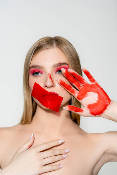 Young woman with red adhesive tape on mouth and paint on hand isolated on grey  - Foto, immagini