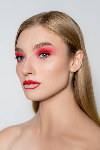 Young model with naked shoulder and red makeup looking away isolated on grey  - Photo, Image