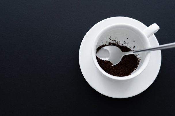 bovenaanzicht van gemalen koffie in kopje met lepel op zwart  - Foto, afbeelding