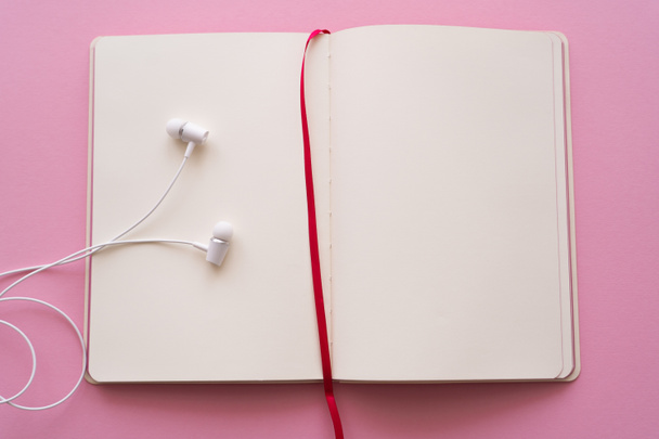 top view of open notebook and wired earphones on pink  - 写真・画像