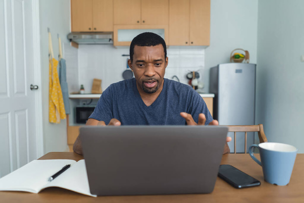 Afro american businessman working on laptop computer at home. Black freelancer guy speaking virtual video conference meeting with colleagues people, video call due to social distancing at home office. - 写真・画像