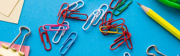 close up view of colorful paper clips near pencil on blue, banner - Valokuva, kuva