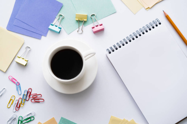 top view of cup of coffee near blank notebook and colorful stationery on white - Photo, Image