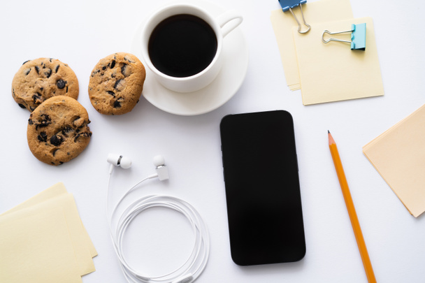 top view of cup of coffee and chocolate chip cookies near stationery and smartphone on white - Valokuva, kuva