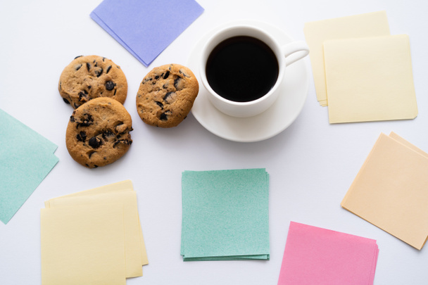 top view of chocolate chip cookies and cup of coffee near paper notes on white - Foto, afbeelding