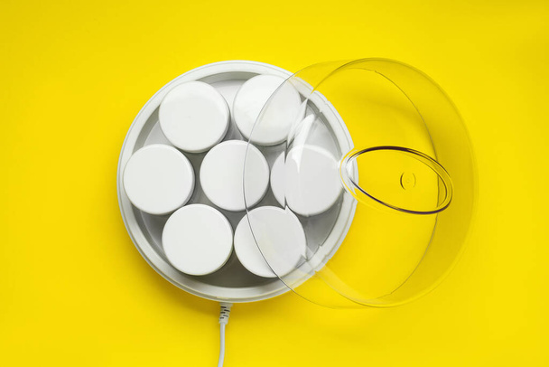 Modern yogurt maker with jars on yellow background, top view - 写真・画像