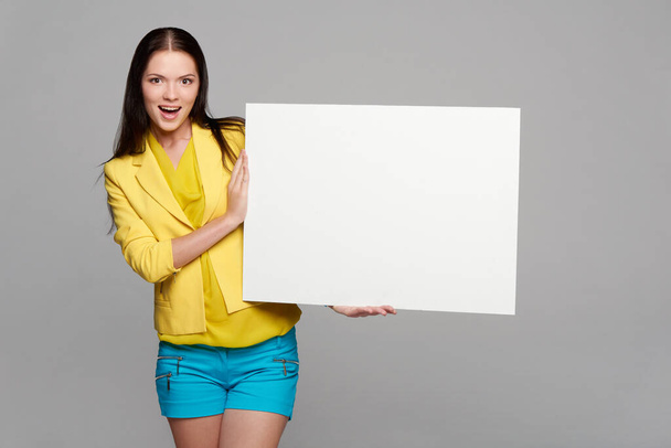 Happy excited girl in yellow and blue, holding empty whiteboard - Фото, зображення