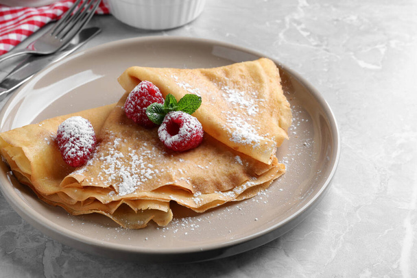 Delicious crepes served with mint, raspberries and powdered sugar on grey table, closeup - Foto, Imagem