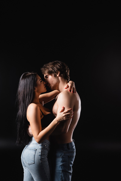 Side view of sexy couple in jeans kissing and hugging isolated on black  - Fotó, kép