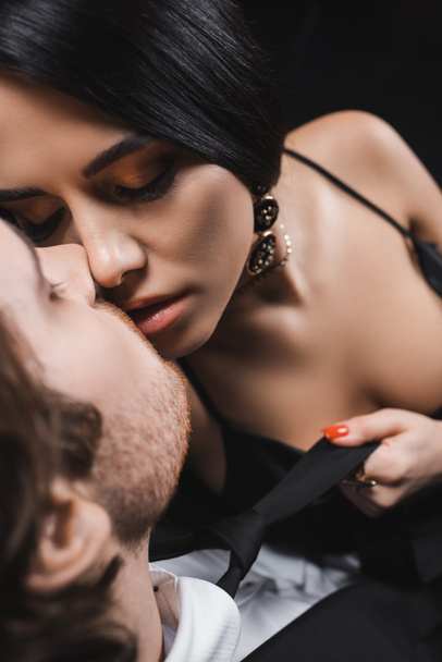 Top view of seductive woman kissing boyfriend in suit isolated on black  - Fotó, kép