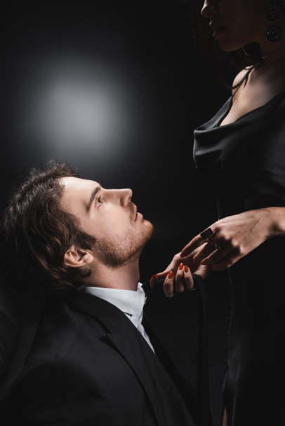 Side view of man in suit looking at sensual girlfriend in silk dress on black background - Foto, Imagen