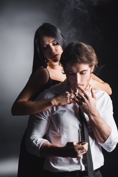 Sensual woman touching boyfriend smoking cigarette on black background - Foto, immagini