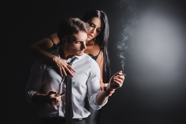 Sexy woman touching boyfriend with lighter and cigarette on black background - Photo, Image