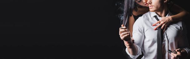 Cropped view of sexy woman touching boyfriend in shirt holding lighter and cigarette on black background, banner  - Foto, afbeelding