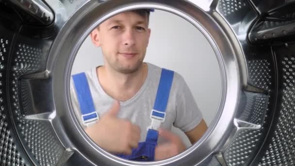 Bir ev aletleri yıkama makinesi remommer yanıtlayıcısı çamaşır makinesinin içine bakar ve parmağını işaret ederek iyi ya da iyi işaret eder. Sınıf. Bir sürü iş yapıldı. Hizmet adamları. - Video, Çekim