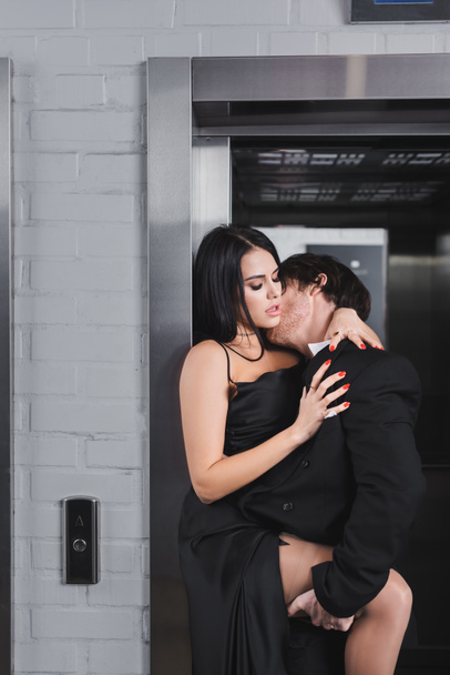 Brunette man in suit kissing sexy woman in dress near elevator  - Photo, Image