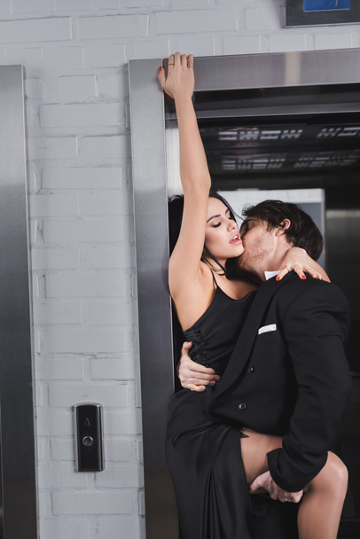 Young man in suit kissing sensual woman in dress near elevator  - Foto, Imagem
