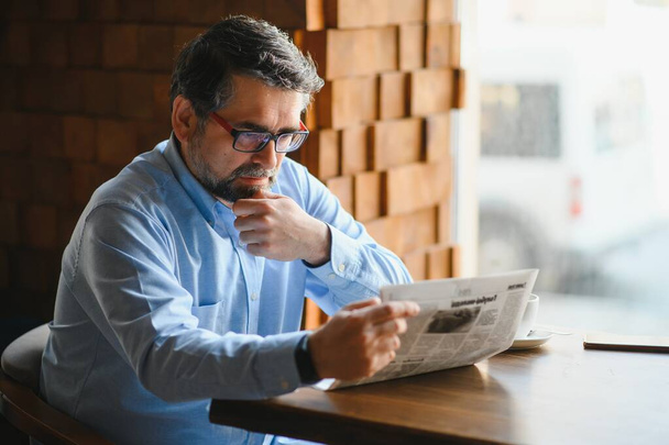 active senior man reading newspaper and drinking coffee in restaurant. - Photo, Image