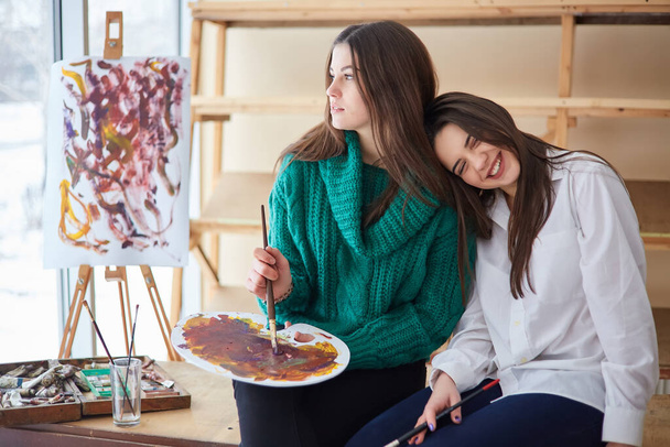 Δύο νεαρά κορίτσια, μελαχρινές ζωγραφίζουν μια ελαιογραφία σε ένα εργαστήριο τέχνης. - Φωτογραφία, εικόνα
