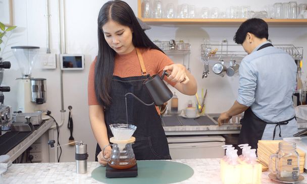 Jonge vrouw die coffeeshop ondernemer schenkt warm water om drift koffie te maken in een modern cafe. - Foto, afbeelding