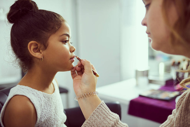 Shes a little pageant princess. Shot of a stylist applying makeup to a cute little girl in a dressing room. - Foto, afbeelding