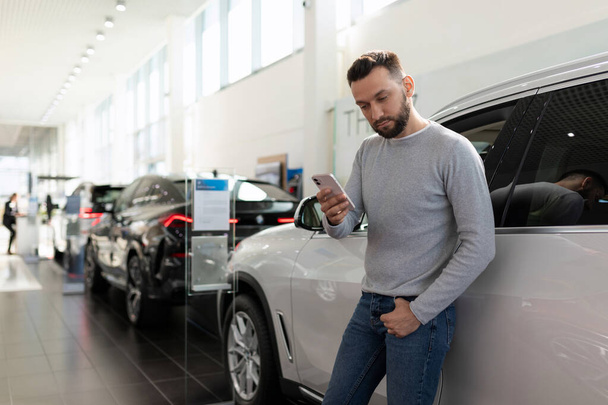 un hombre estudia la oferta de las compañías de seguros en un concesionario de automóviles en un teléfono inteligente - Foto, Imagen