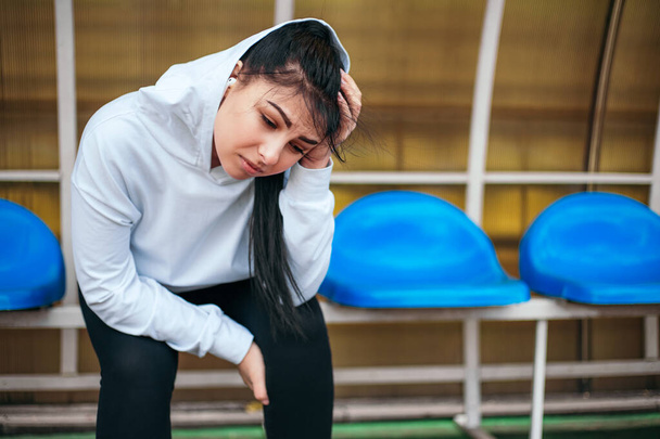 Young woman sitting at the stadium with upset sad mood. She has no desire for training or jogging, crying. - Photo, Image
