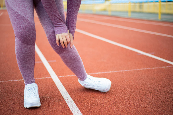 Urheilullinen nainen pukeutunut urheilupuku on polvivammoja harjoitellessaan lenkkeily tekee urheilua stadionilla käynnissä juoksumatto. Naisurheilija tuntee kipua, murtunut nyrjähtänyt nivel - Valokuva, kuva