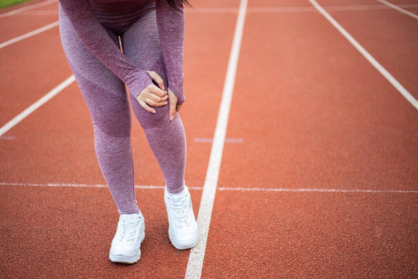 スポーツスーツを着たスポーティ女性は、陸上トラックトレッドミルでスポーツをやってジョギングを実行するトレーニング中に膝の損傷を持っています。女性アスリートは痛みを感じ、関節を捻挫 - 写真・画像