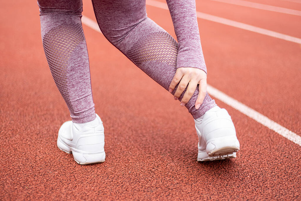 Sporty woman dressed sports suit have ankle injury while training running jogging doing sport at the stadium running track treadmill. Female athlete feel pain, broken sprained huckle bone muscle - Photo, Image