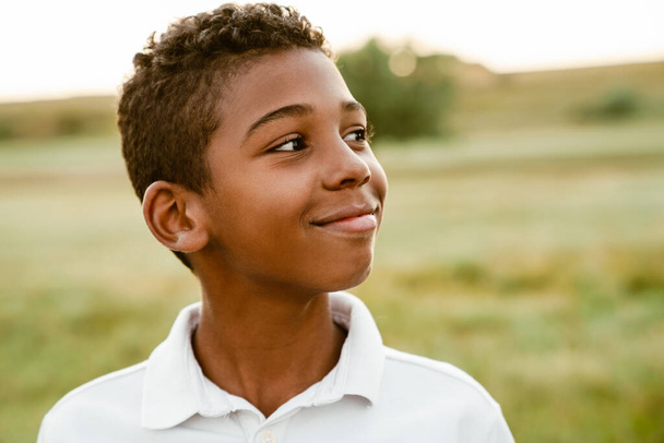 Black boy wearing white shirt smiling and looking aside while posing outdoors - Foto, afbeelding