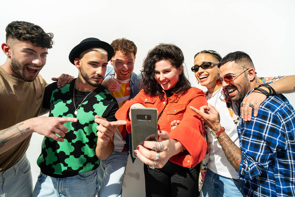 Group of multiracial young fashionable friends using cell phone, making selfie and sharing content on social media. People spending time together, having fun outdoor. Friendship. Real people lifestyle - Zdjęcie, obraz