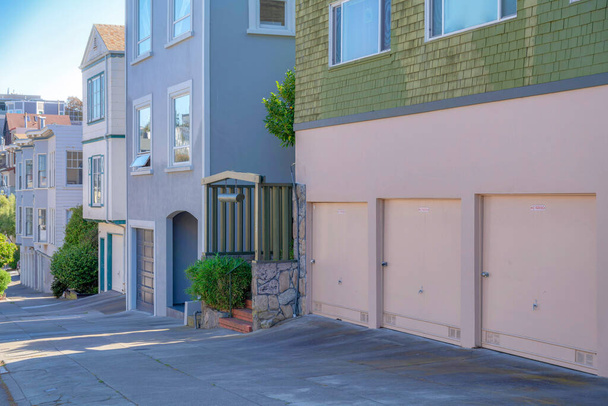 San Franciscon asuinrakennukset kaltevalla kadulla Kaliforniassa. On rivi taloja alkaen talon oikealla vihreä päre sivuraide ja kolme autotallin ovet. - Valokuva, kuva