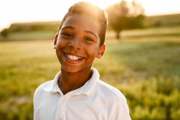 Black boy wearing white shirt smiling and looking at camera while posing outdoors - Fotó, kép